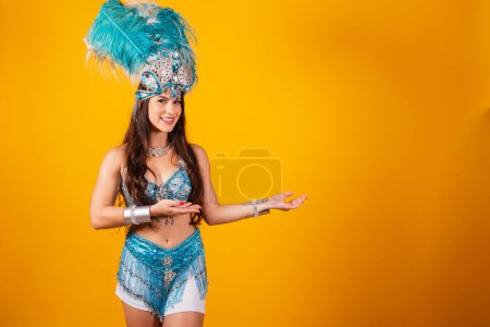 Téléchargez les photos : Belle femme brésilienne avec des vêtements de reine de l'école de samba, carnaval. Couronne de plumes, présentant quelque chose sur la droite. - en image libre de droit
