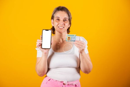 Photo for Adult Brazilian woman holding driver's license and smartphone with green screen - Royalty Free Image