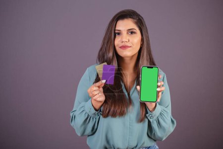 Photo for Horizontal photo. Beautiful Brazilian woman, with casual clothes, Jeans and green shirt. smartphone with green screen and cards. - Royalty Free Image