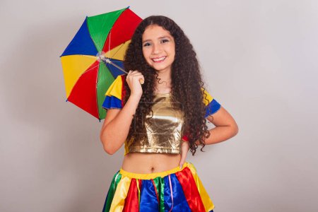 Foto de Jovencita adolescente, brasileña, con ropa frevo, carnaval. con paraguas y las manos en la cintura. - Imagen libre de derechos
