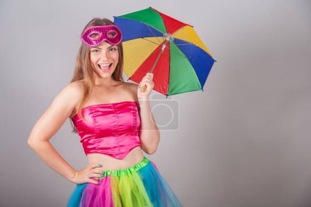 Téléchargez les photos : Femme blonde brésilienne vêtue de vêtements de carnaval rose. portant un masque, avec un parapluie frevo. - en image libre de droit