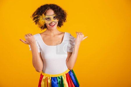 Téléchargez les photos : Belle femme brésilienne, vêtue de vêtements de carnaval, jupe colorée et chemise blanche. portant un mascara, invitant avec les mains. - en image libre de droit