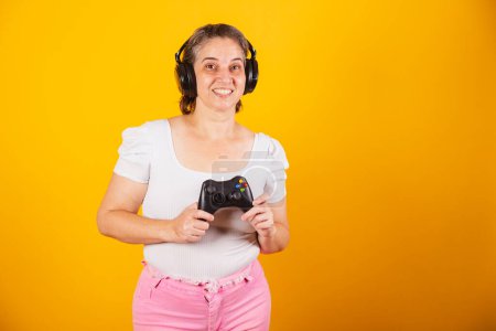 Foto de Mujer brasileña adulta, madre, sosteniendo control remoto de videojuegos, joystick. Gamer. usando auriculares, jugando en línea. - Imagen libre de derechos