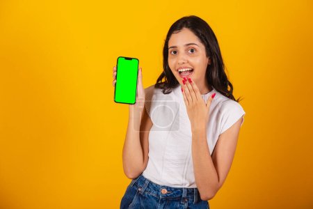 Foto de Hermosa mujer brasileña sosteniendo teléfono inteligente, mostrando pantalla de croma verde. - Imagen libre de derechos