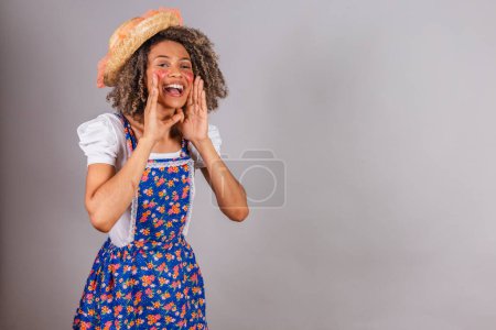 Foto de Joven brasileña negra, con ropa de campo, vestida para Festa Junina. Festival de San Juan. promoción gritando, publicidad. - Imagen libre de derechos