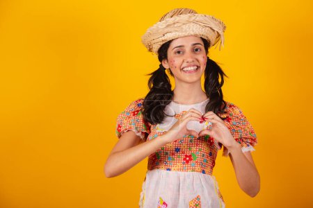 Téléchargez les photos : Femme brésilienne, dans les vêtements de la fête junina, signe du coeur avec les mains. - en image libre de droit