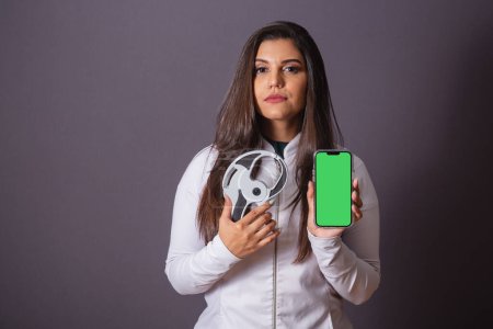 Téléchargez les photos : Photo horizontale. femme brésilienne avec manteau médical, nutritionniste. adipomètre et smartphone, écran vert. minceur. - en image libre de droit