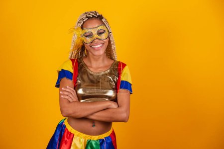 Photo for Beautiful black Brazilian woman, dressed in carnival clothes, mask. yellow background. crossed arms. - Royalty Free Image
