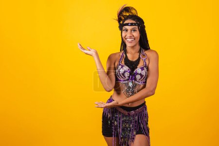 Foto de Hermosa mujer brasileña negra, en ropa de carnaval púrpura, presentando algo a un lado. anuncio. - Imagen libre de derechos