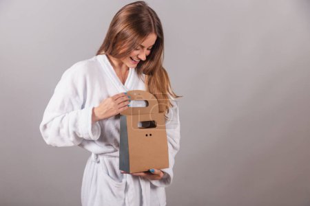 Photo for Brazilian blonde woman showing wonderful hair. dressed in a robe. holding cardboard bag with cosmetics and hair - Royalty Free Image