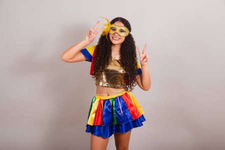 Téléchargez les photos : Jeune adolescente, brésilienne, avec des vêtements frevo, carnaval. masque, signe de paix et d'amour pose pour photo. - en image libre de droit