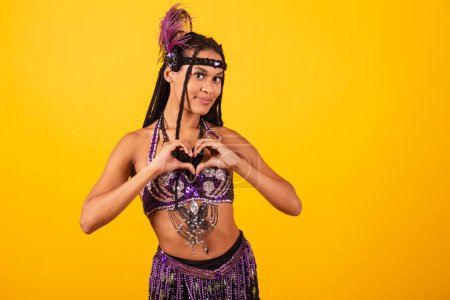 Téléchargez les photos : Belle femme brésilienne noire, avec des vêtements de carnaval violet, signe du coeur avec les mains. - en image libre de droit