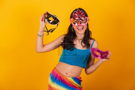 Photo for Beautiful brazilian woman in carnival clothes, wearing carnival mask and holding two masks, smiling. - Royalty Free Image