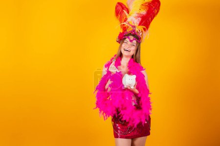Foto de Hermosa mujer brasileña rubia con ropa de reina de la escuela de samba, carnaval. Corona de plumas. tenencia de alcancía y moneda. - Imagen libre de derechos