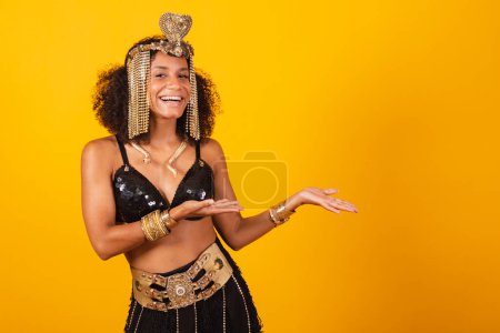 Photo for Beautiful black Brazilian woman, in Cleopatra carnival clothes, presenting something to the right. - Royalty Free Image