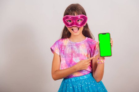 Téléchargez les photos : Belle fille brésilienne, enfant, habillée pour le carnaval au Brésil. montrant smartphone avec écran Chroma vert. - en image libre de droit