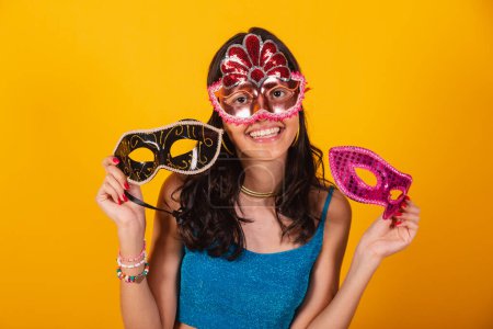Téléchargez les photos : Belle femme brésilienne en vêtements de carnaval, portant un masque de carnaval et tenant deux masques, souriant. - en image libre de droit