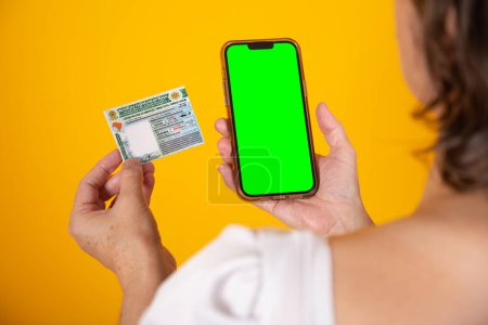 Photo for Hand holding Brazilian car and vehicle driving license, CNH, smartphone with green screen - Royalty Free Image