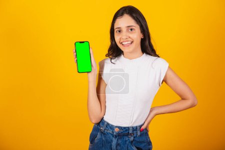 Photo for Beautiful brazilian woman holding smartphone, showing green chroma screen. - Royalty Free Image
