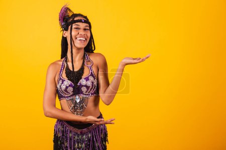 Téléchargez les photos : Belle femme brésilienne noire, vêtue de carnaval violet, présentant quelque chose sur le côté. annonce. - en image libre de droit