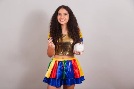Foto de Jovencita adolescente, brasileña, con ropa frevo, carnaval. tenencia de alcancía y moneda. - Imagen libre de derechos