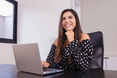 Photo for Beautiful Brazilian woman, entrepreneur, in office, using notebook and smartphone, working. - Royalty Free Image