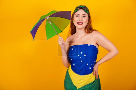 Téléchargez les photos : Belle rousse brésilienne avec des vêtements de carnaval fabriqués avec le drapeau du Brésil, et parasol coloré. - en image libre de droit