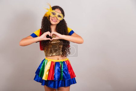Photo for Young teen girl, brazilian, with frevo clothes, carnival. mask, heart sign with hands. - Royalty Free Image