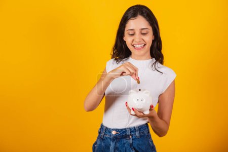 Photo for Beautiful brazilian woman holding piggy bank and coin. - Royalty Free Image