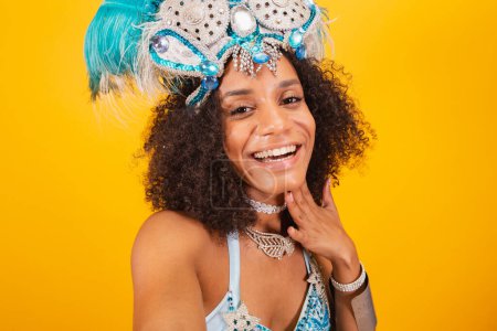 Foto de Mujer negra reina de la escuela brasileña de samba, con ropa de carnaval azul y corona de plumas. sosteniendo máscara. autorretrato con smartphone. - Imagen libre de derechos