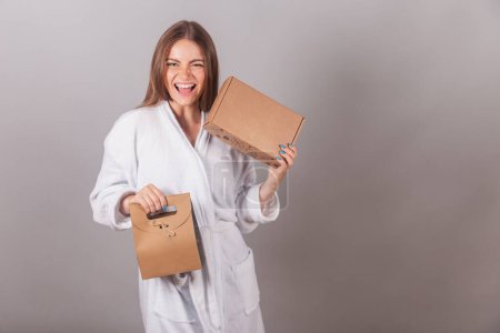 Photo for Brazilian blonde woman showing wonderful hair. dressed in a robe. holding shopping bag and cardboard box with cosmetics. - Royalty Free Image