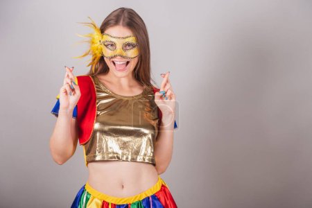 Foto de Mujer rubia brasileña, vestida con ropa frevo, máscara de carnaval, signo de la suerte con los dedos, deseando. - Imagen libre de derechos