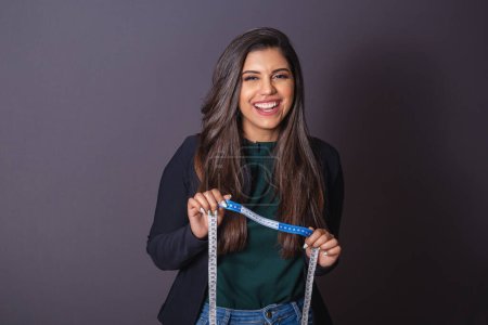 Photo for Horizontal photo. Beautiful Brazilian woman in casual clothes, black blazer jeans. holding measuring tape, nutritionist. - Royalty Free Image