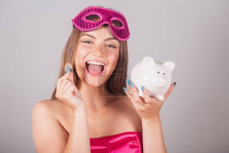 Téléchargez les photos : Femme blonde brésilienne vêtue de vêtements de carnaval rose. tenant tirelire et monnaie. Économisez. investir. - en image libre de droit