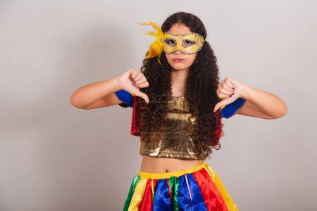Téléchargez les photos : Jeune adolescente, brésilienne, avec des vêtements frevo, carnaval. masque, signe de dégoût avec les doigts. - en image libre de droit