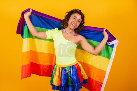 Foto de Hermosa mujer brasileña afroamericana, en ropas de carnaval, sosteniendo bandera lgbt. Orgullo gay. - Imagen libre de derechos