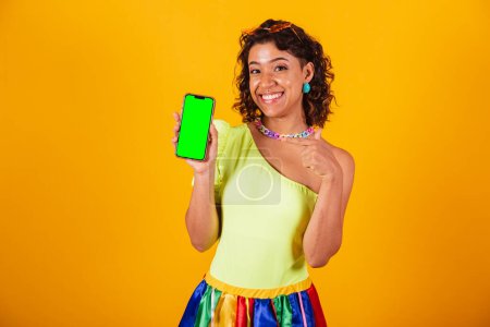 Téléchargez les photos : Belle femme brésilienne afro-américaine, en vêtements de carnaval, tenant smartphone avec écran vert en chroma. - en image libre de droit