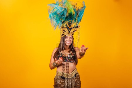 Téléchargez les photos : Belle femme brésilienne en vêtements de carnaval d'or, portant la couronne de plumes de danseur de carnaval. invitant avec les mains - en image libre de droit