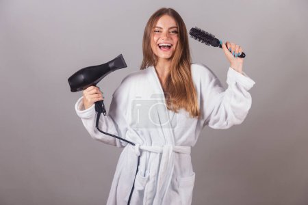 Photo for Brazilian blonde woman showing wonderful hair. dressed in a robe. using hair dryer and hairbrush. - Royalty Free Image