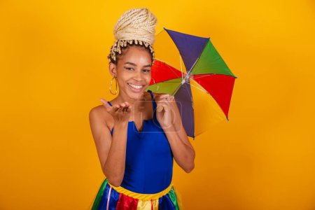 Téléchargez les photos : Belle femme brésilienne noire, vêtue de vêtements de carnaval, fond bleu et jaune, pain et tresses, parapluie frevo. Embrasser signe. - en image libre de droit