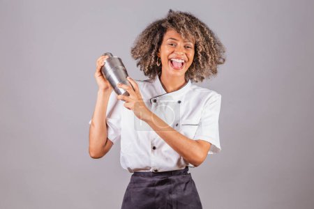 Photo for Young black Brazilian woman, cook, masterchef, wearing restaurant uniform. holding cocktail shaker for preparing drinks. - Royalty Free Image