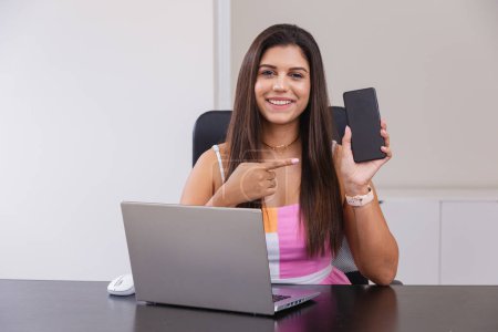 Téléchargez les photos : Belle femme d'affaires brésilienne caucasienne travaillant dans le bureau, montrant téléphone portable. - en image libre de droit