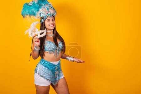 Téléchargez les photos : Belle femme brésilienne en bleu et blanc vêtements de carnaval. avec couronne de plumes et masque présentant le produit ou le texte sur le côté. annonce. - en image libre de droit