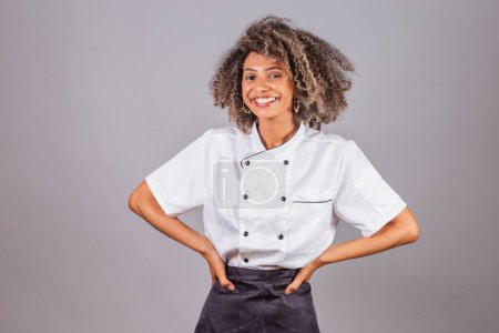 Foto de Joven brasileña negra, cocinera, masterchef, vistiendo uniforme de restaurante. Manos en las caderas. - Imagen libre de derechos
