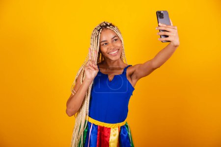 Foto de Hermosa mujer negra, brasileña con trenzas, con ropa para el carnaval. Sostiene el smartphone. autorretrato. - Imagen libre de derechos