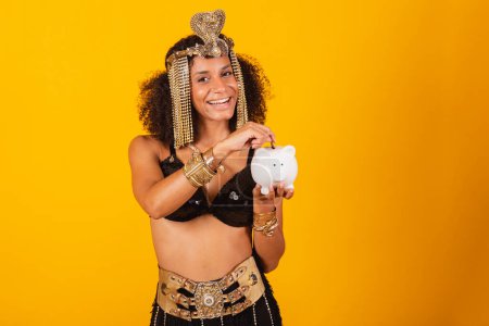 Foto de Hermosa mujer negra brasileña, en ropa de carnaval Cleopatra, sosteniendo alcancía y moneda. - Imagen libre de derechos