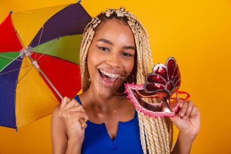 Photo for Beautiful black Brazilian woman, dressed in carnival clothes, blue, and yellow background, holding umbrella and mask. - Royalty Free Image