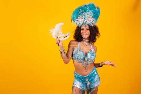 Photo for Black woman queen of Brazilian samba school, with blue carnival clothes and crown of feathers. holding mask. welcome. - Royalty Free Image