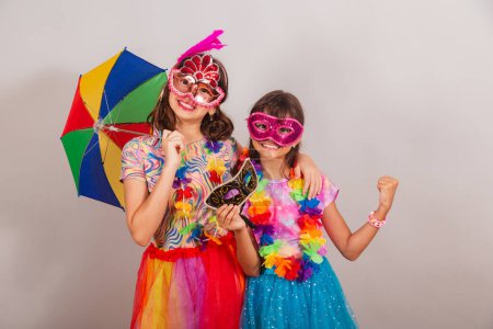 Photo for Two brazilian children, girls, friends, dressed in carnival clothes, holding smartphone, app, mobile. - Royalty Free Image
