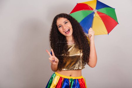 Photo for Young teen girl, brazilian, with frevo clothes, carnival. with umbrella sign of peace and love. - Royalty Free Image